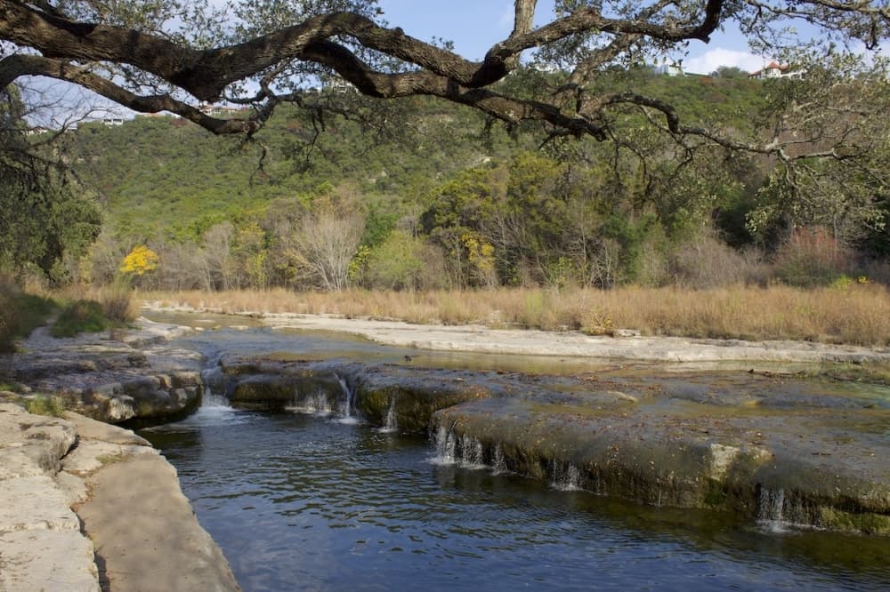 small creek with watering hole at the end and hills behind it covered in trees