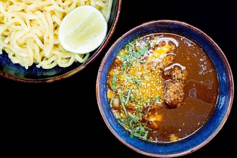A plate with noodles and lemon with a bowl of meat and broth