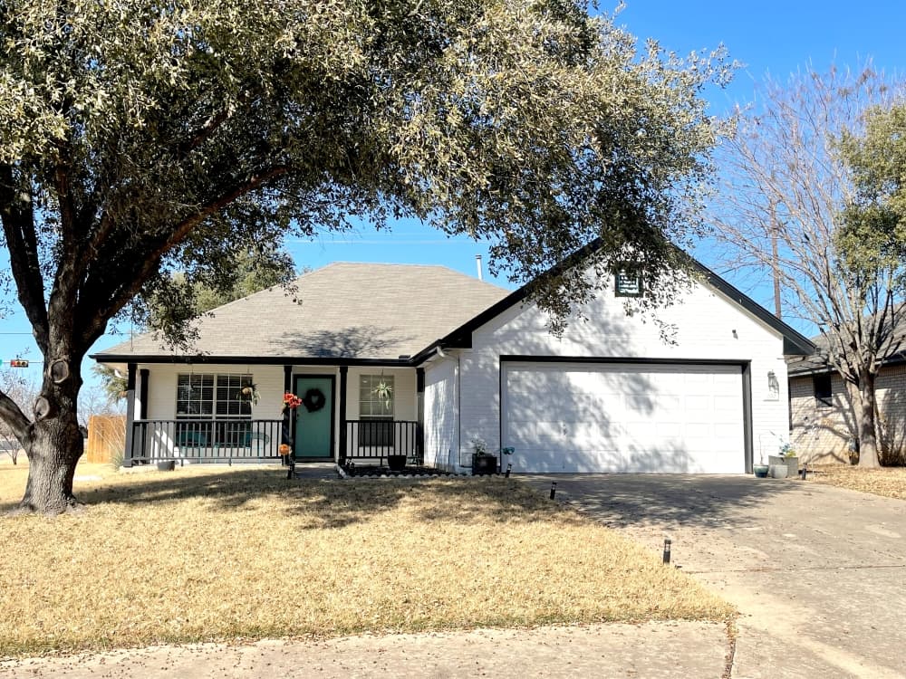 home in katy crossing has white paint and black trim with large tree in the front yard
