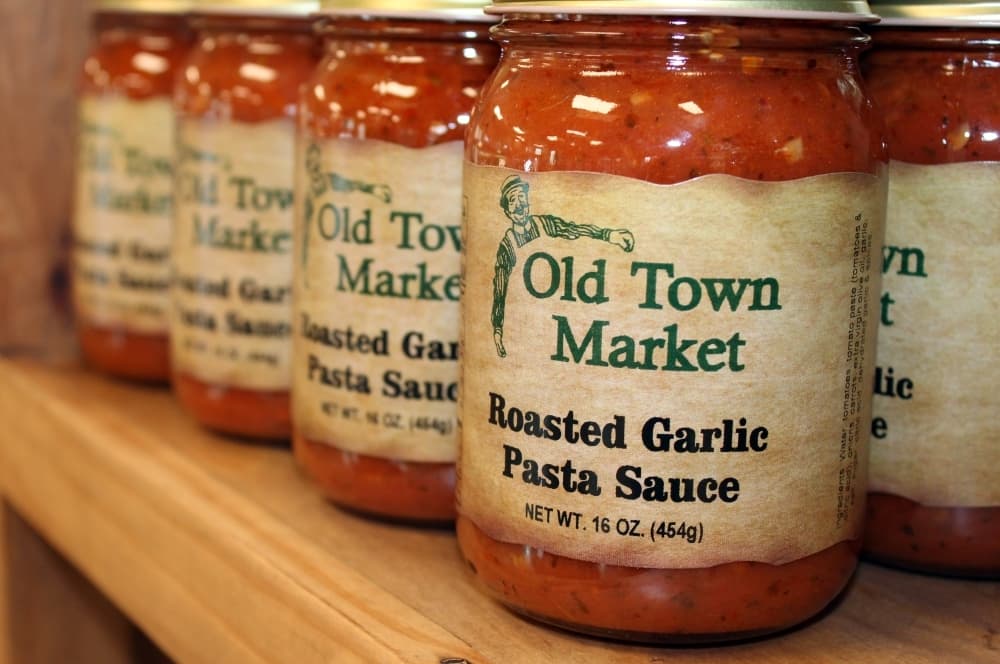 Jars of pasta sauce sit on a shelf in a store. 