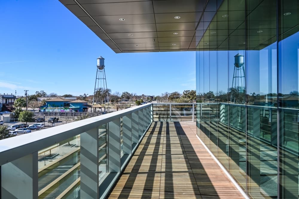 outdoor patio with wooden floors, white railing and glass walls has views of round rock including water tower 