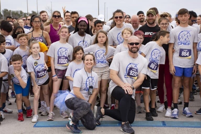 crowd of people smile for a photo wearing the same white tshirt with blue logo