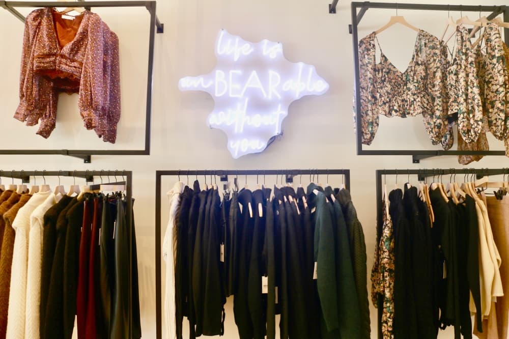 womens clothing hands on the wall around a neon sign that reads "life would be unBEARable without you"