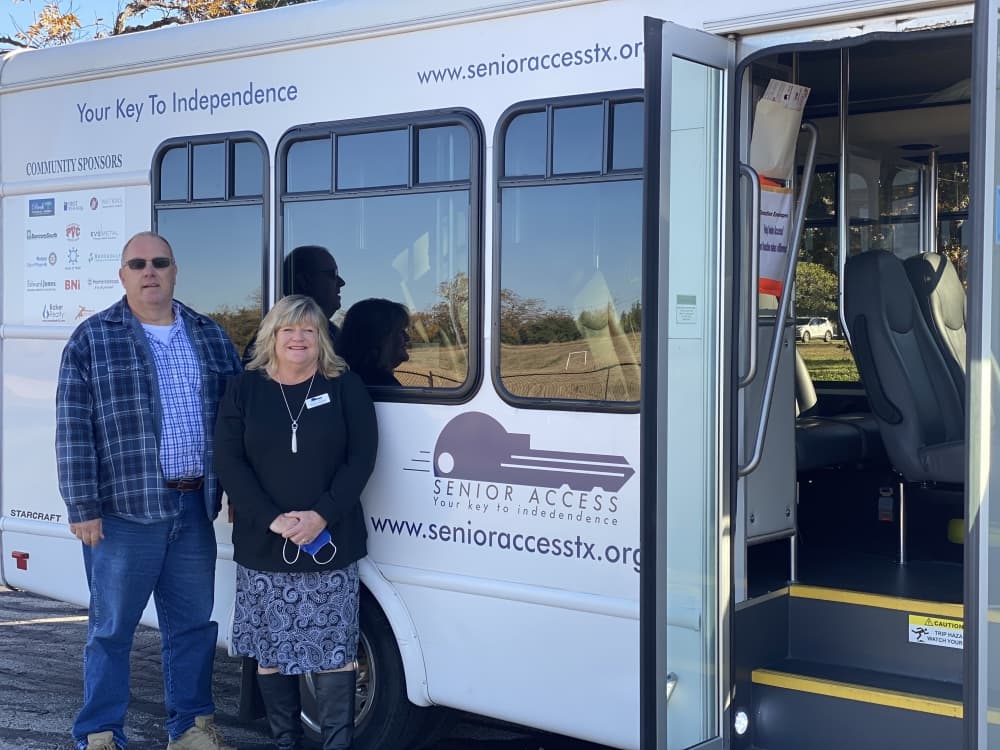 man and woman stand outside white bus 