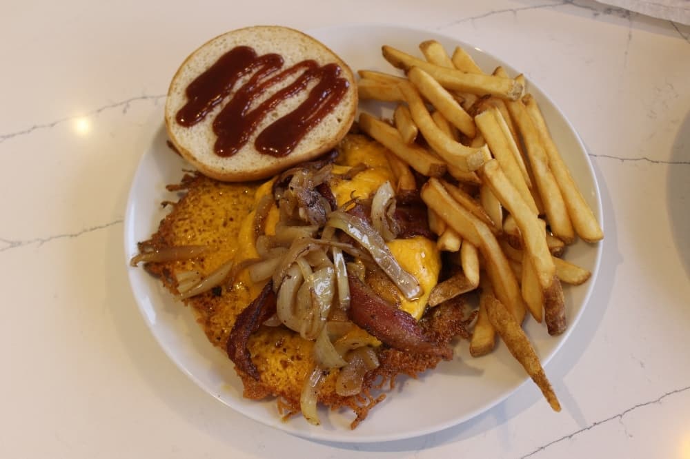 Hunger Crush Burger ($14.95) is served as an overflow burger layered with cheese and the burger comes with a side of fries. (Peyton MacKenzie/Community Impact)