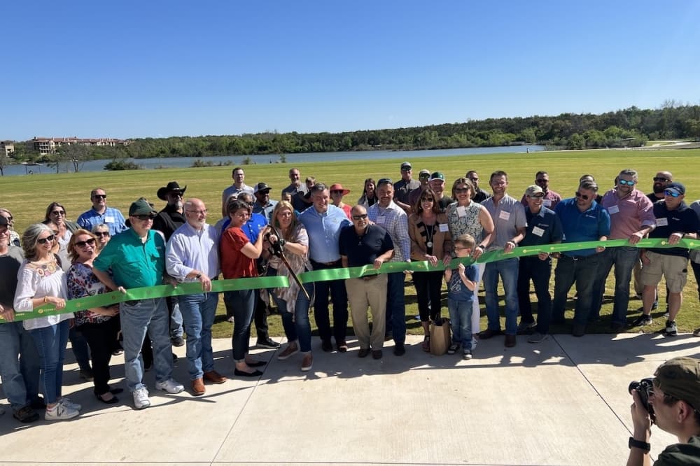 a crowd of people standing behind a large ribbon with two people toward the center holding a large pair of scissors and cutting the ribbon