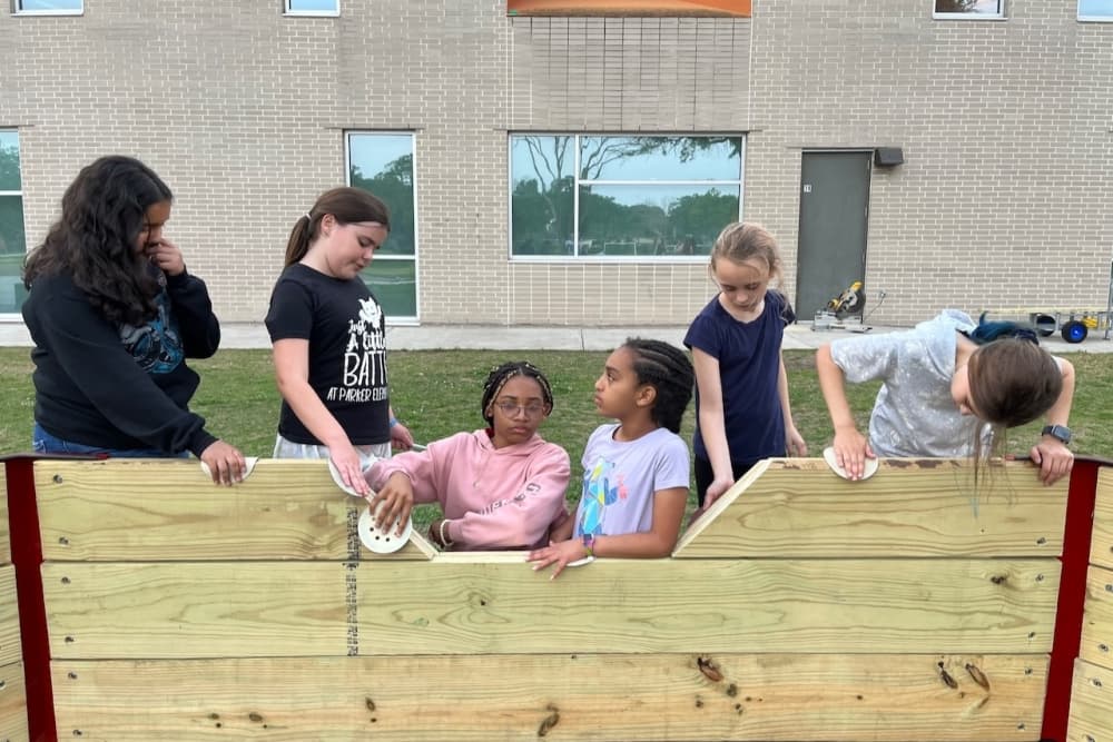 Girls stand together in a Gaga Ball pit being built