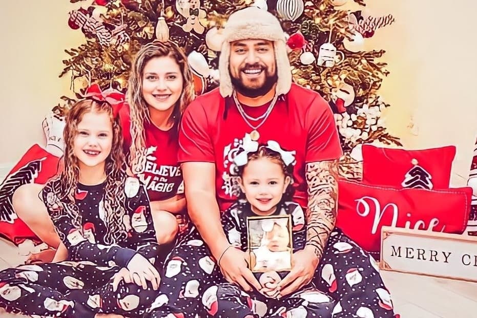 Amber Latu and family pose for a picture around their Christmas tree, with her husband holding a photo of their late daughter Journey.