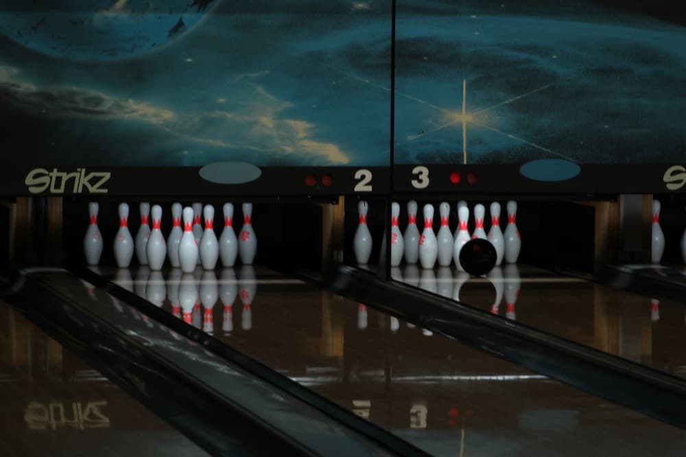 a bowling ball rolls into pins at Strikz