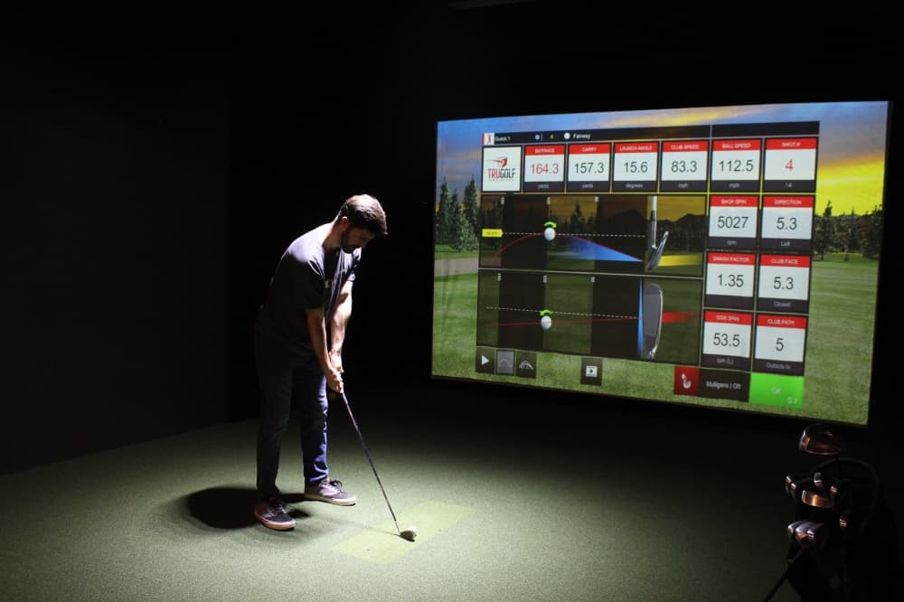 Man holding golf club in front of golf simulator screen with swing analysis data