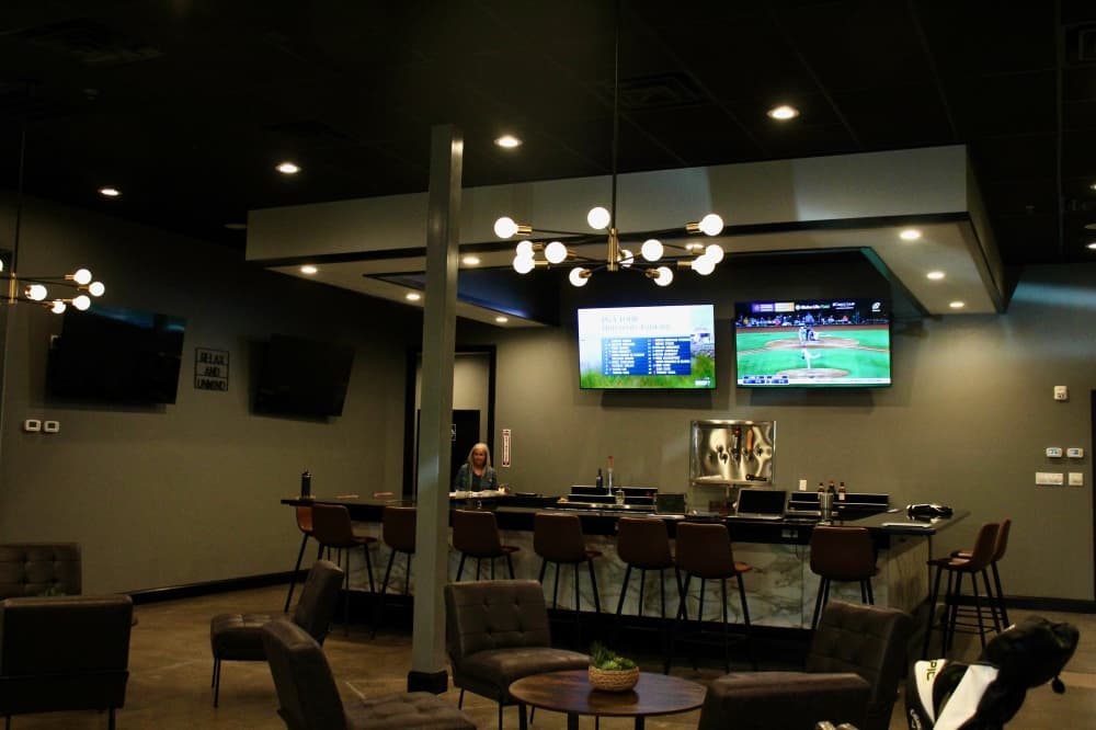Interior of The Clubhouse Indoor Golf with tables, chairs, a bar and TV's