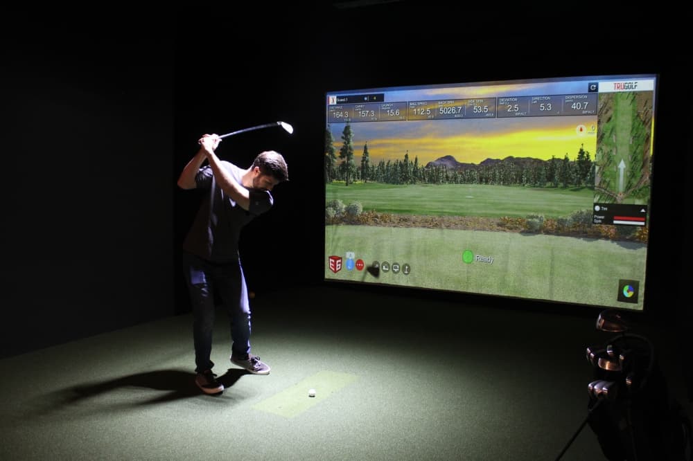 Man swinging golf club on gold simulator 