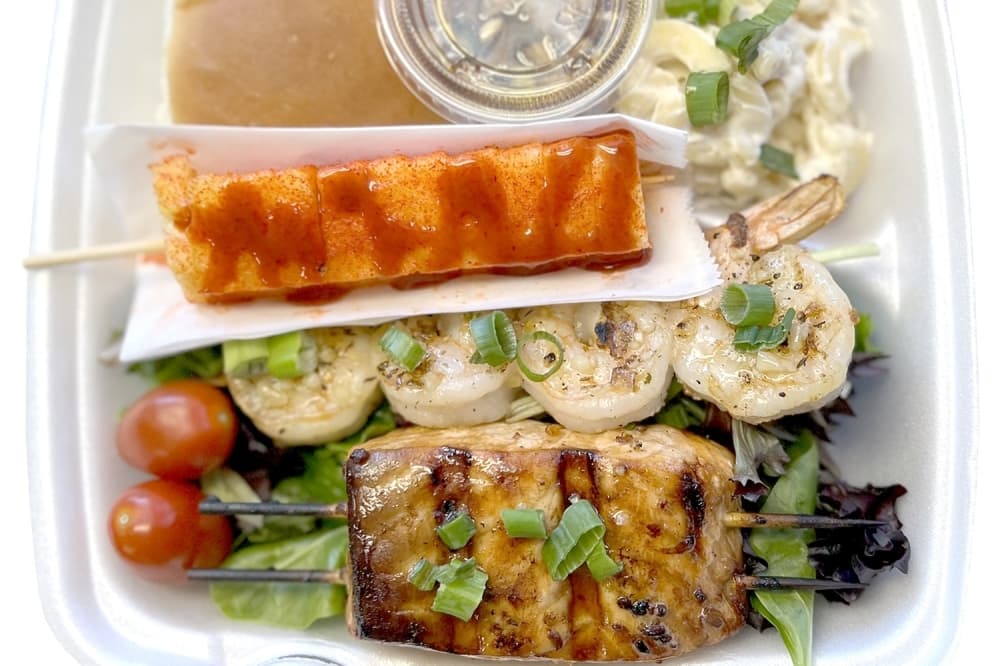 A Plate No. 2 with grilled garlic butter shrimp, adobo-seasoned salmon, mixed greens salad, fresh pineapple with li hing mui and chamoy, mac salad, Hawaiian roll and finadene sauce. (Zacharia Washington/Community Impact)