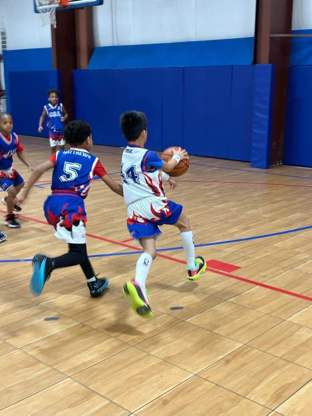 Two kids running with a basketball on a court