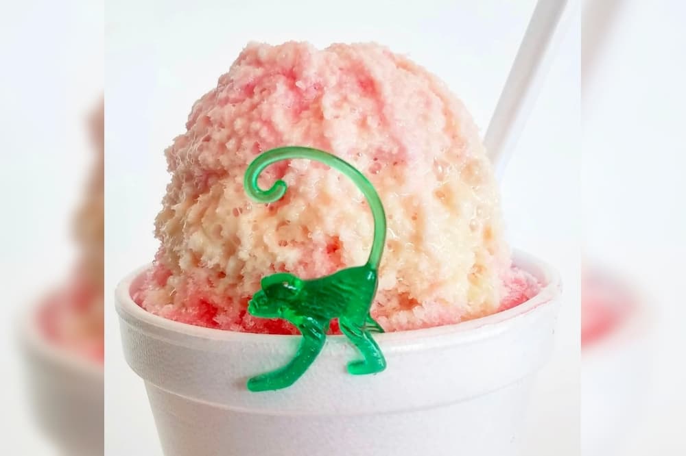 Snow cone with red syrup and ice cream and a green monkey on the cup