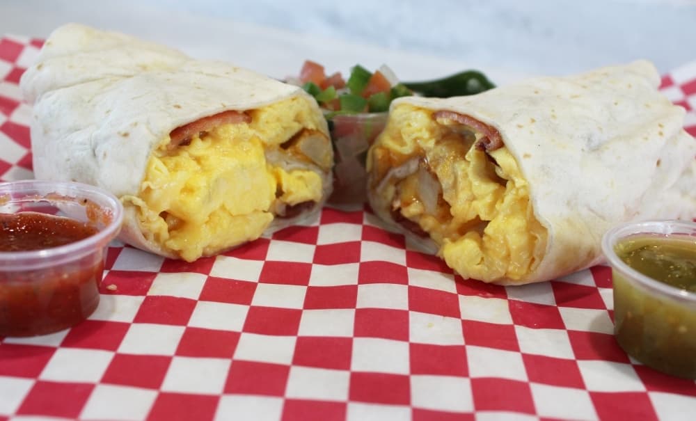 Burrito cut in half filled with eggs, bacon, potatoes and cheese on red and white checkered background