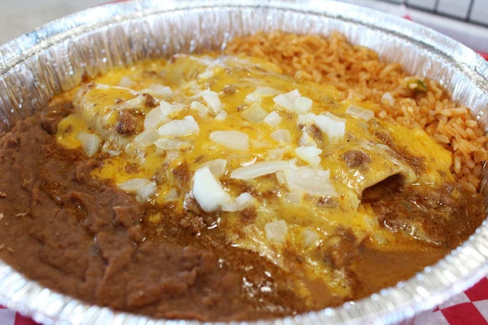 Beef enchiladas smothered in chili con carne sauce served with a side of rice and beans.