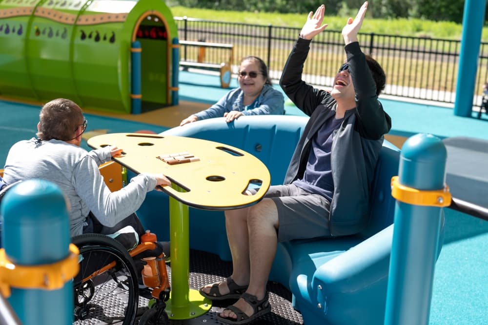 two people, one in a wheelchair, on playground equipment while a third person looks on