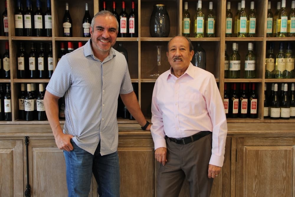 Owners standing in front of wine bottles