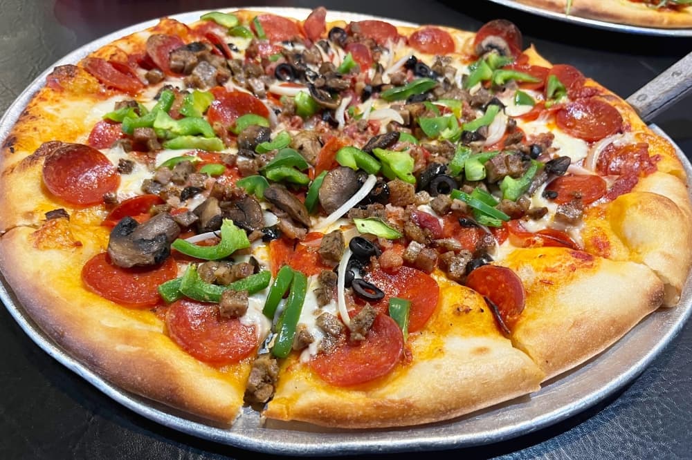 A pizza with pepperoni, bacon, meatballs and olives