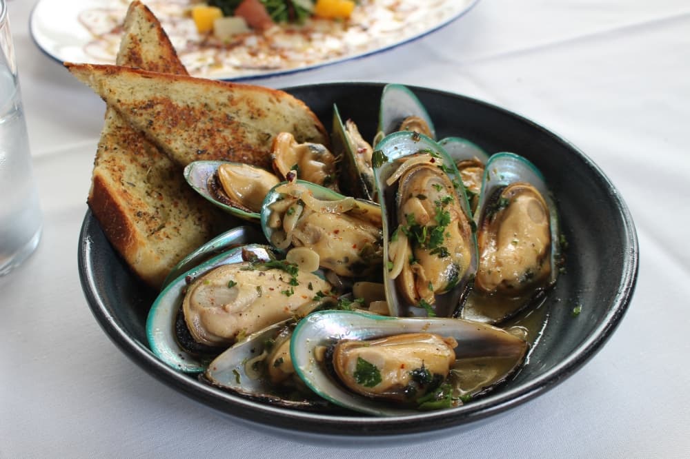 The white wine-steamed mussels ($XX) are served with grilled sourdough and shaved garlic.