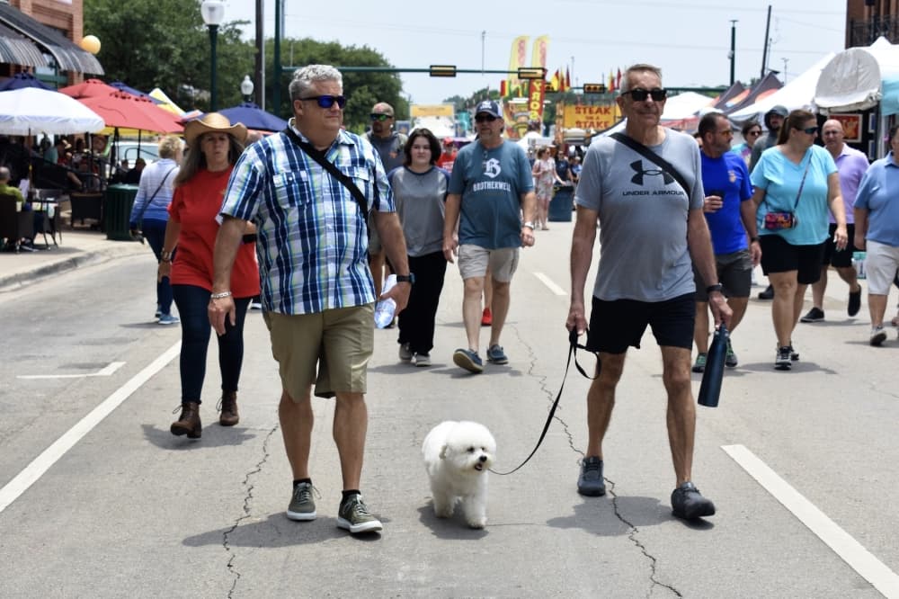 a crowd of people with two men and a white fluffy dog near the front 