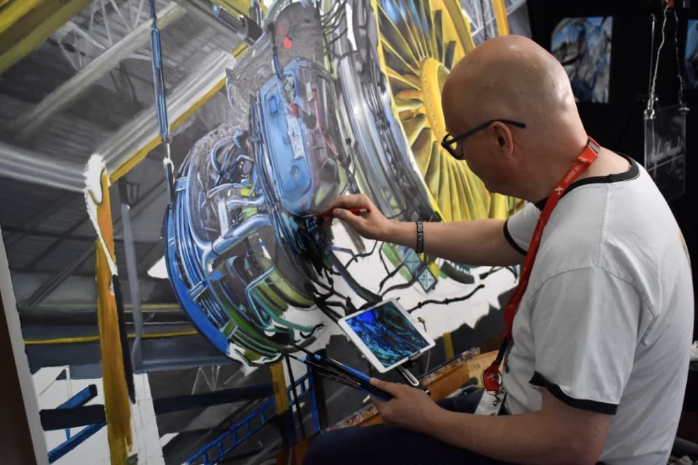 a man sits and paints on a large canvas