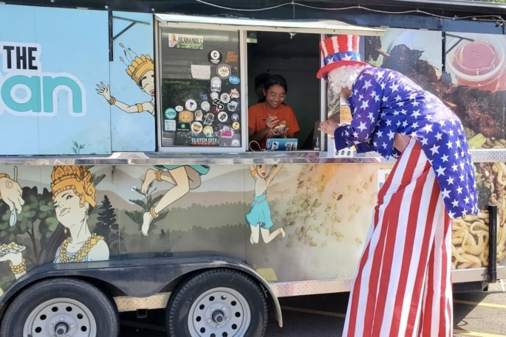 Photo shows a man in an Uncle Sam costume ordering food from a food truck. 