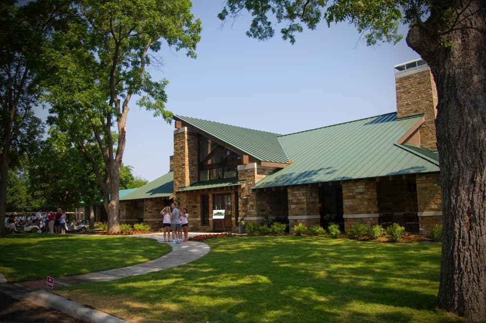 View of exterior of the clubhouse at Oak Hollow Golf Course with people walking and trees