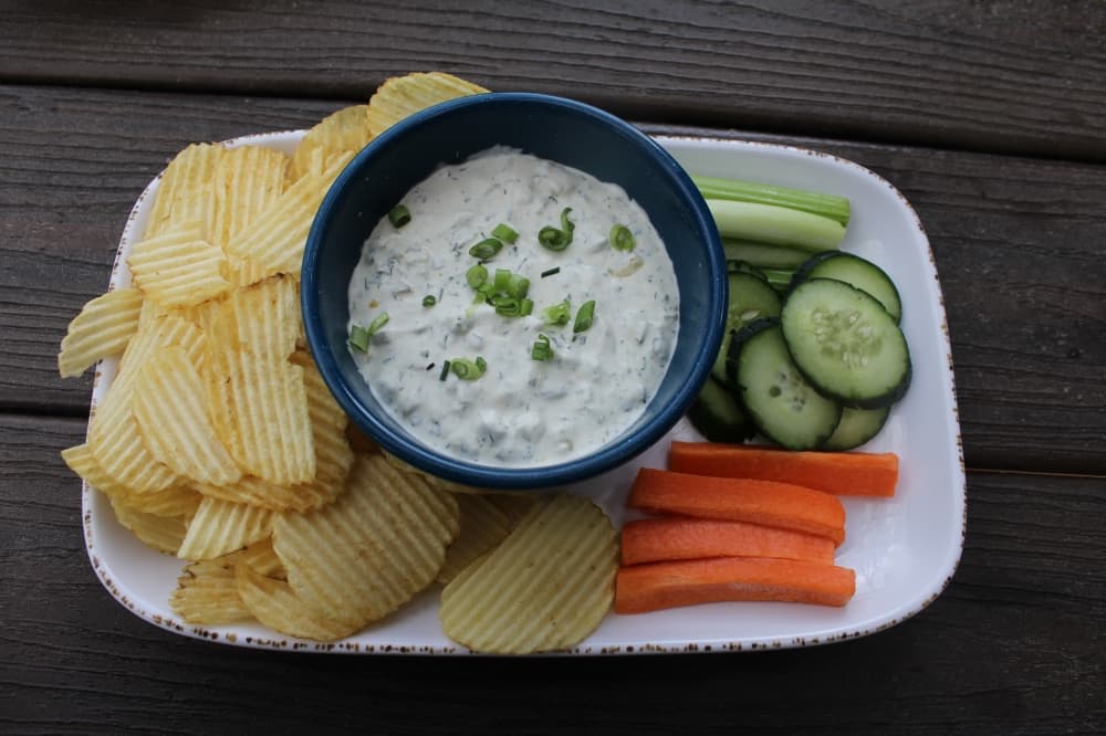 bowl with dip on a plate with chips, carrots, cucumber and celery