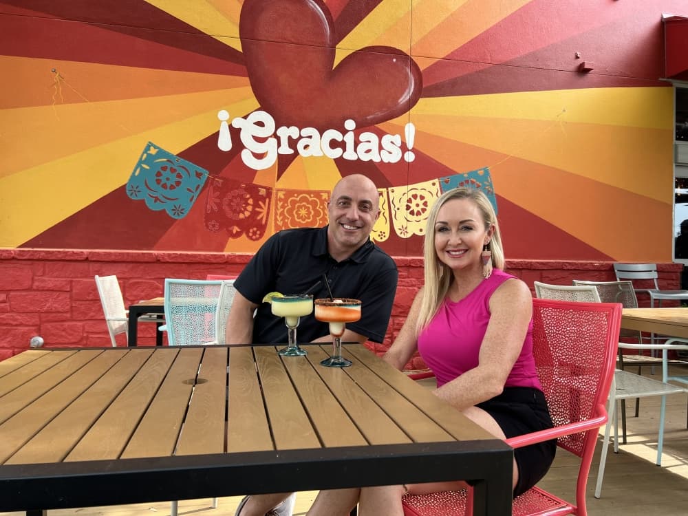 man and woman at table with wall reading "gracias" in the background 