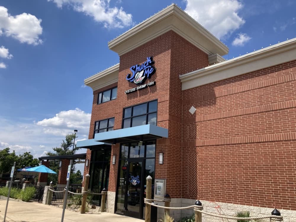 exterior shot of building with red brick and blue sign reading "shuck me" 