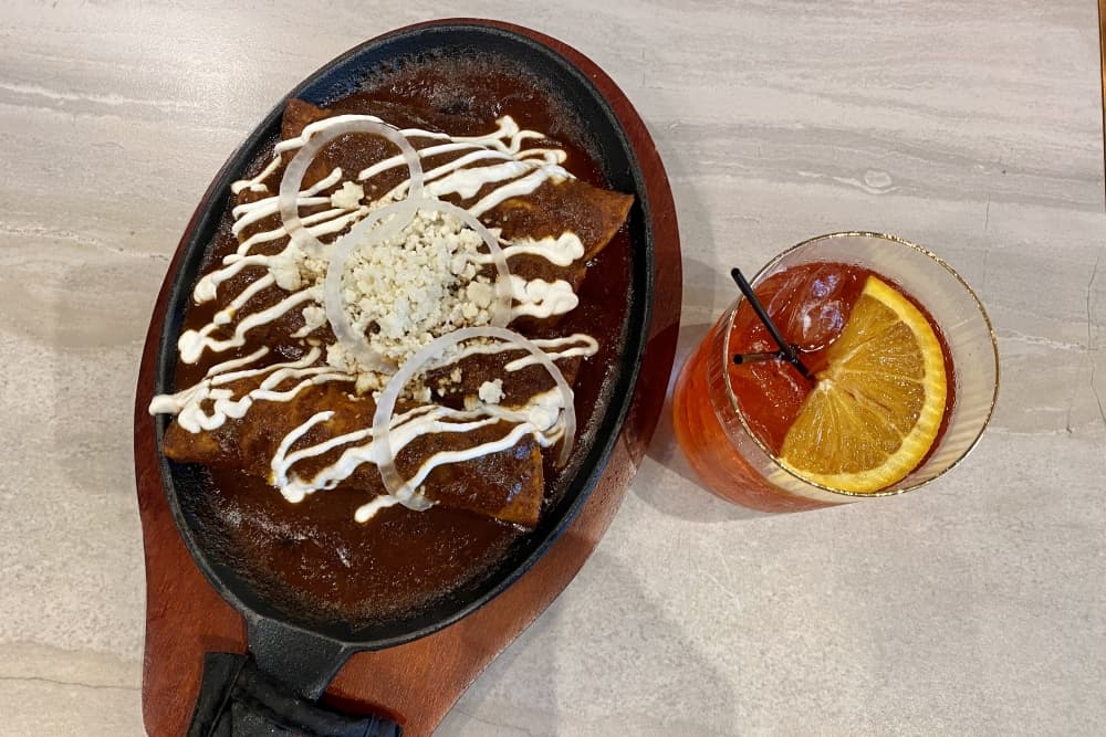 The mole enchiladas ($25) are four corn tortillas stuffed with chicken and topped with mole, sour cream, queso fresco and onion strings. (Cassandra Jenkins/Community Impact)