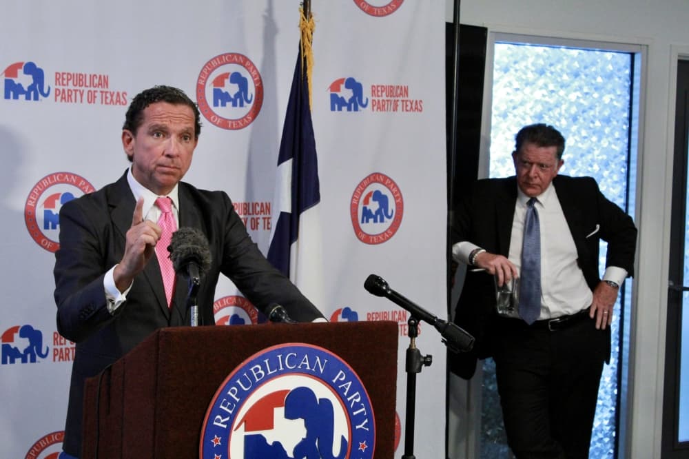 tony buzbee speaks at a podium during a news conference while dan cogdell listens next to the stage area