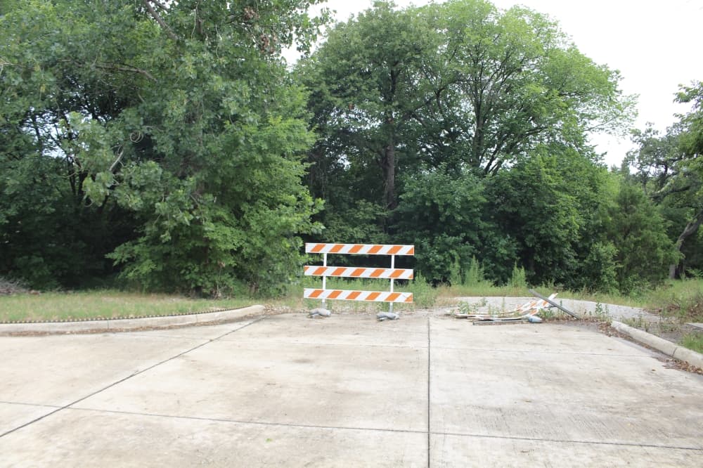 Picture of a road ending with trees and a road barrier as the road stops