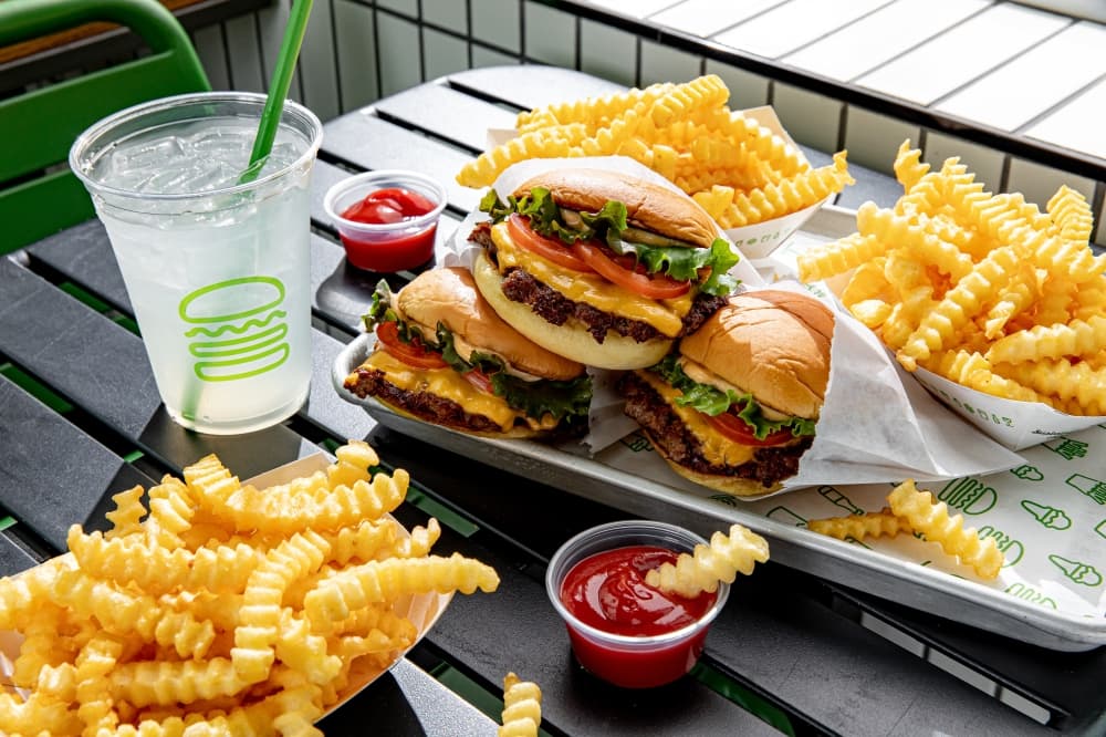 Image of three burgers stacked on top of each other, three bags of fries and two containers of ketchup.