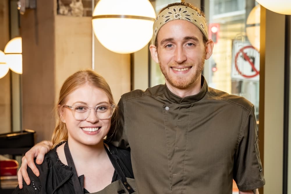 Christine Crossin and Johnny Reyes, owners of Artistry, a new fusion cafe concept coming to Finn Hall in August 2023, pose together with their arms around each other. 