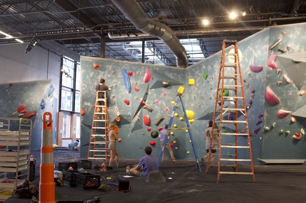 Route Setters with cones and ladders changing the climbing route on a wall.