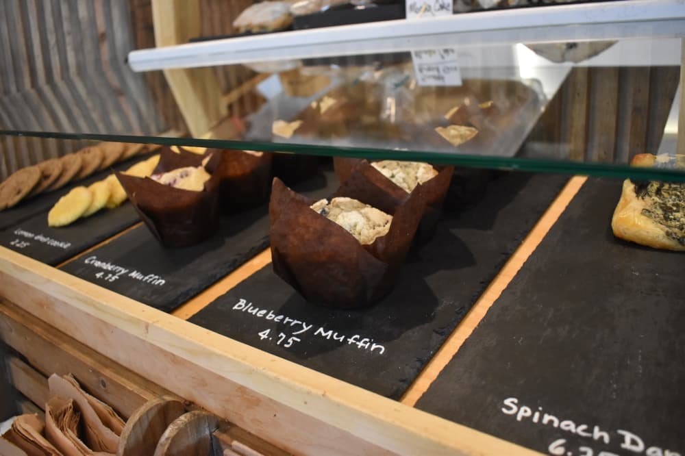 Blueberry muffins sit on a black tray on the pastry counter