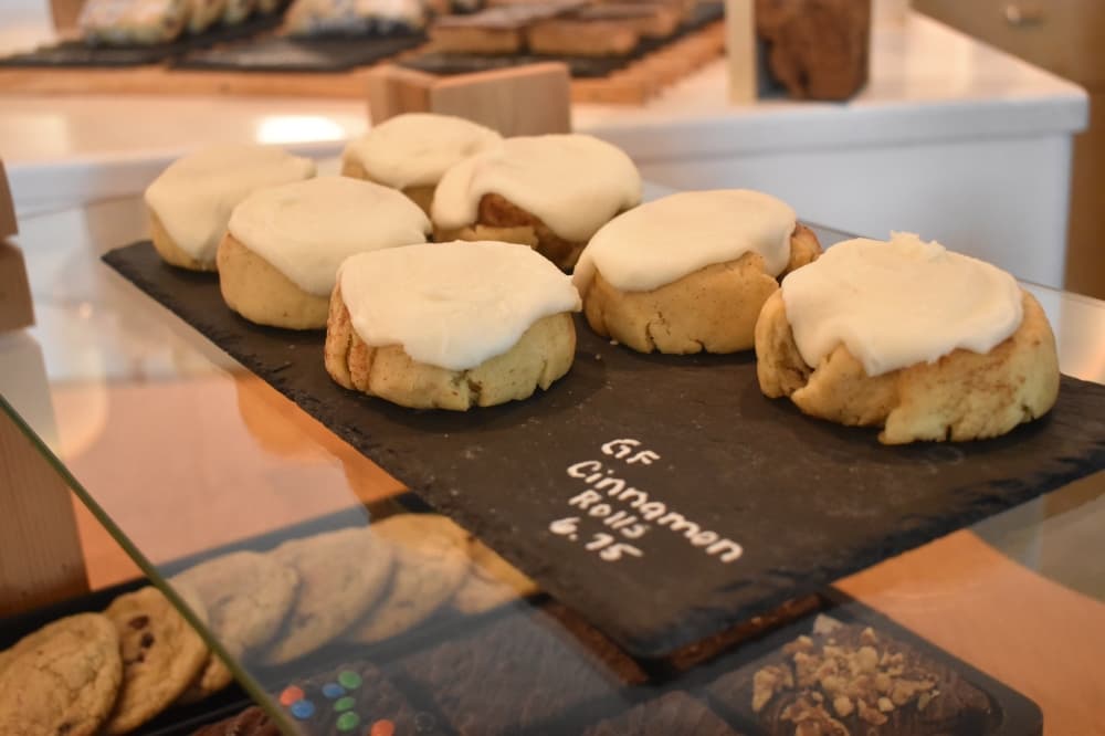 Gluten-free cinnamon rolls sit on a black tray on the pastry counter