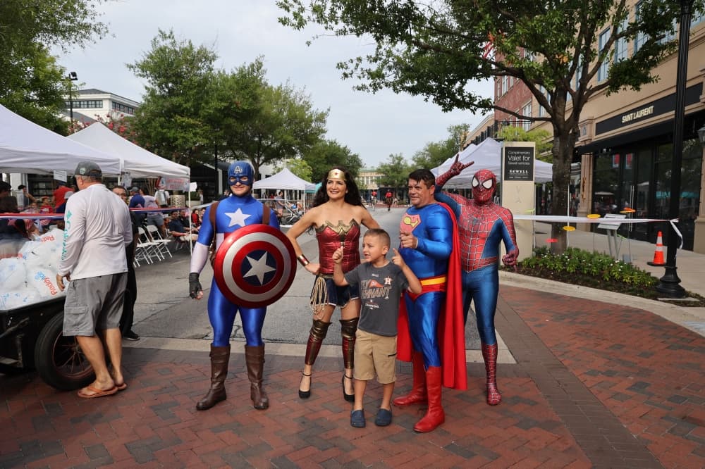 People dresses as popular superheroes like Wonder Woman and Captain America pose with a child.