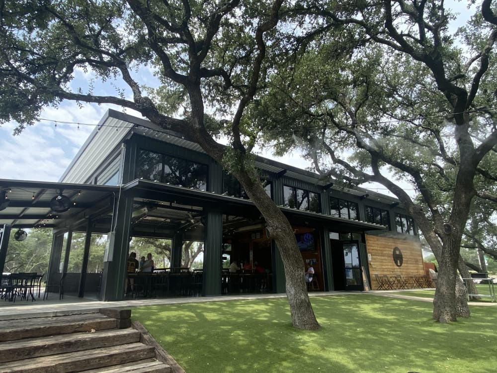 black metal and wood building with shaded seating area and trees 