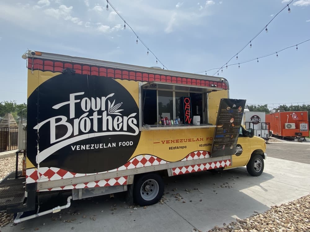 yellow, black and red food truck with "Four Brother Venezuelan Kitchen" sign