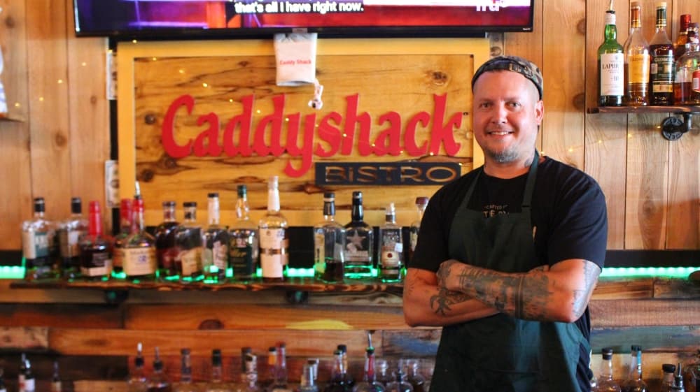 A photo of Austin Schuring standing in front of the Caddy Shack Bistro bar 