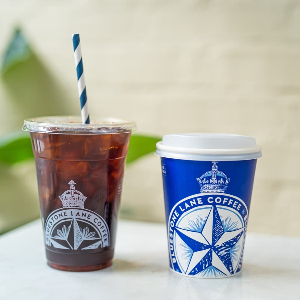 A plastic cup of iced coffee and a blue and white paper cup of coffee.