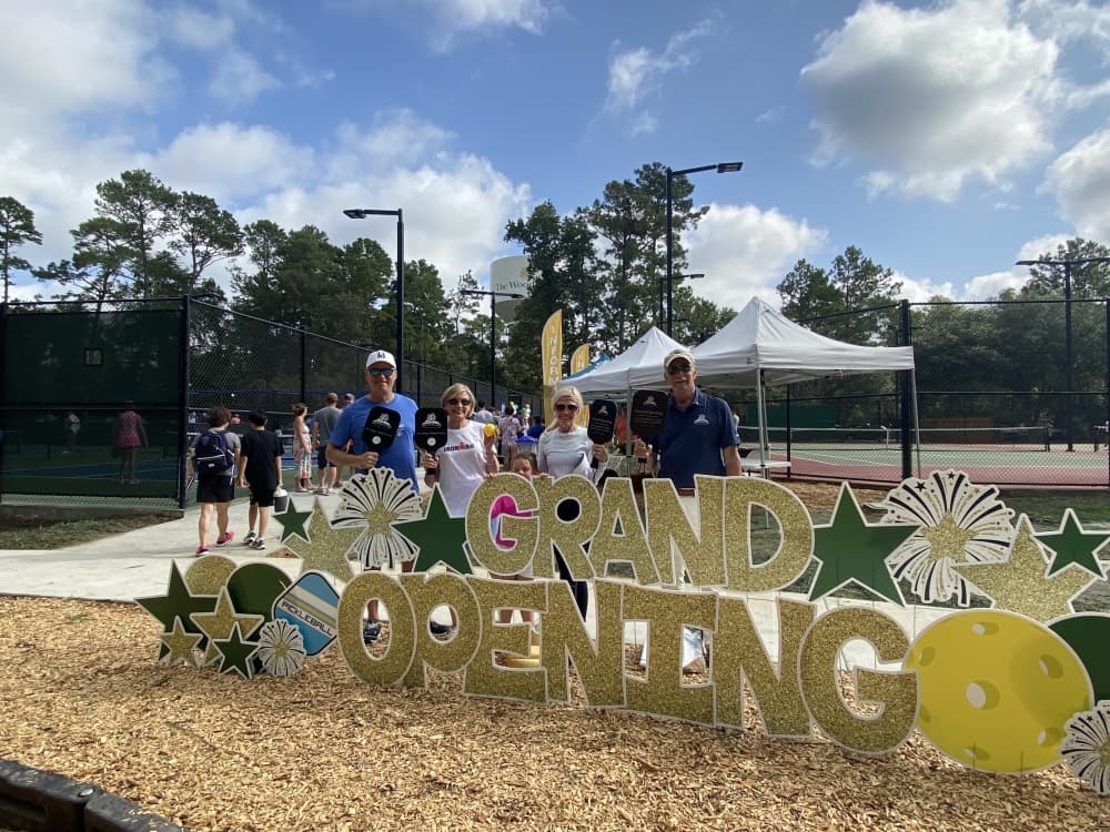 A group of people gather behind an "opening" sign