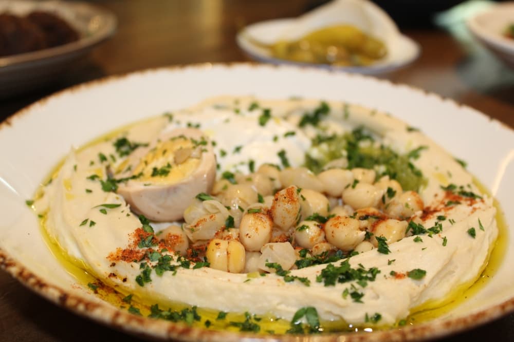 Fresh hummus ($15-$17) is made in-house and available to order for both lunch and dinner, served with pita, olives, onions and pickles. The “hummus complet” is served with chickpeas, tahini and a brown egg. (Melissa Enaje/Community Impact)
