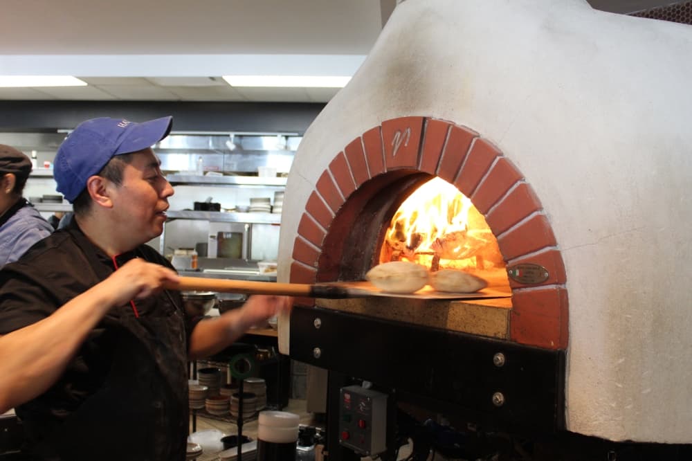 Hamsa staff bakes pita using a wood-burning oven that transforms the housemade dough discs into steaming puffs of pita in a matter of minutes. (Melissa Enaje/Community Impact)