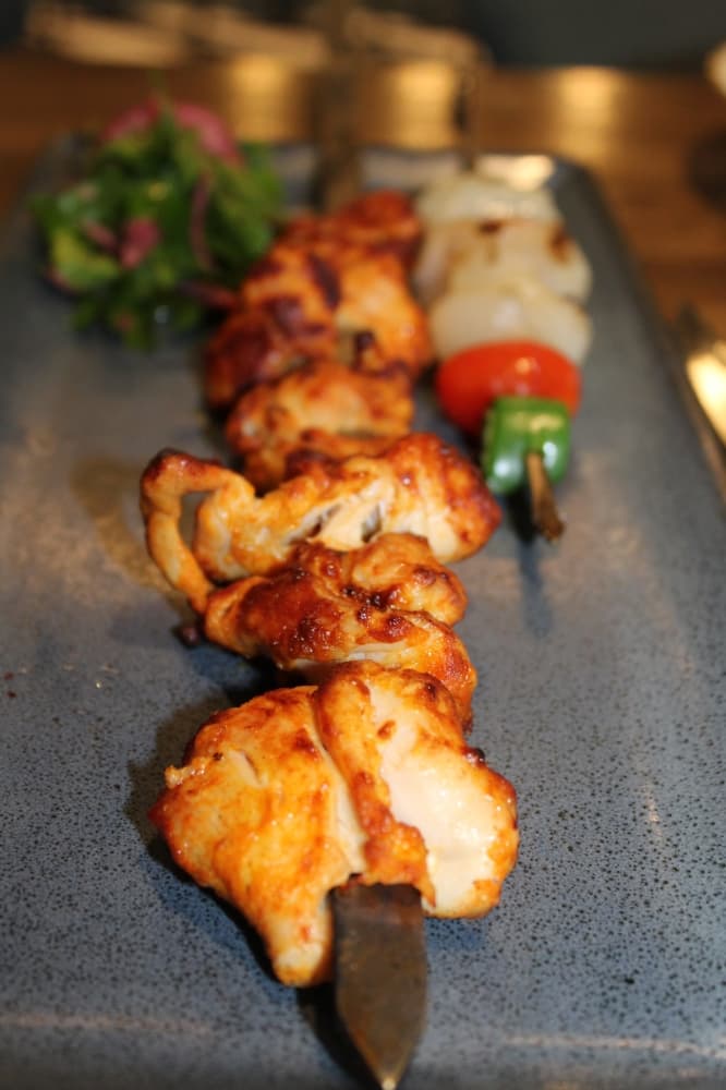 Charcoal-grilled options ($25-$34), such as chicken thighs, are served on a vegetable skewer and paired with a red onion parsley salad. (Melissa Enaje/Community Impact)