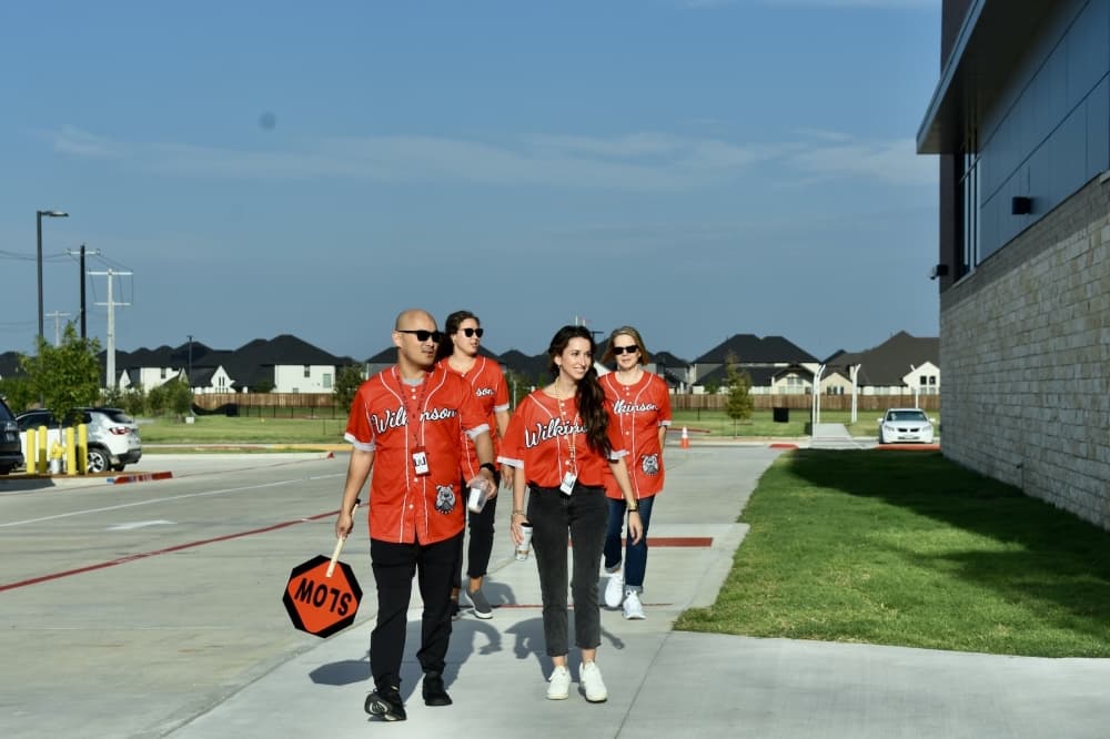four adults walk around a school while holding Slow traffic signs 